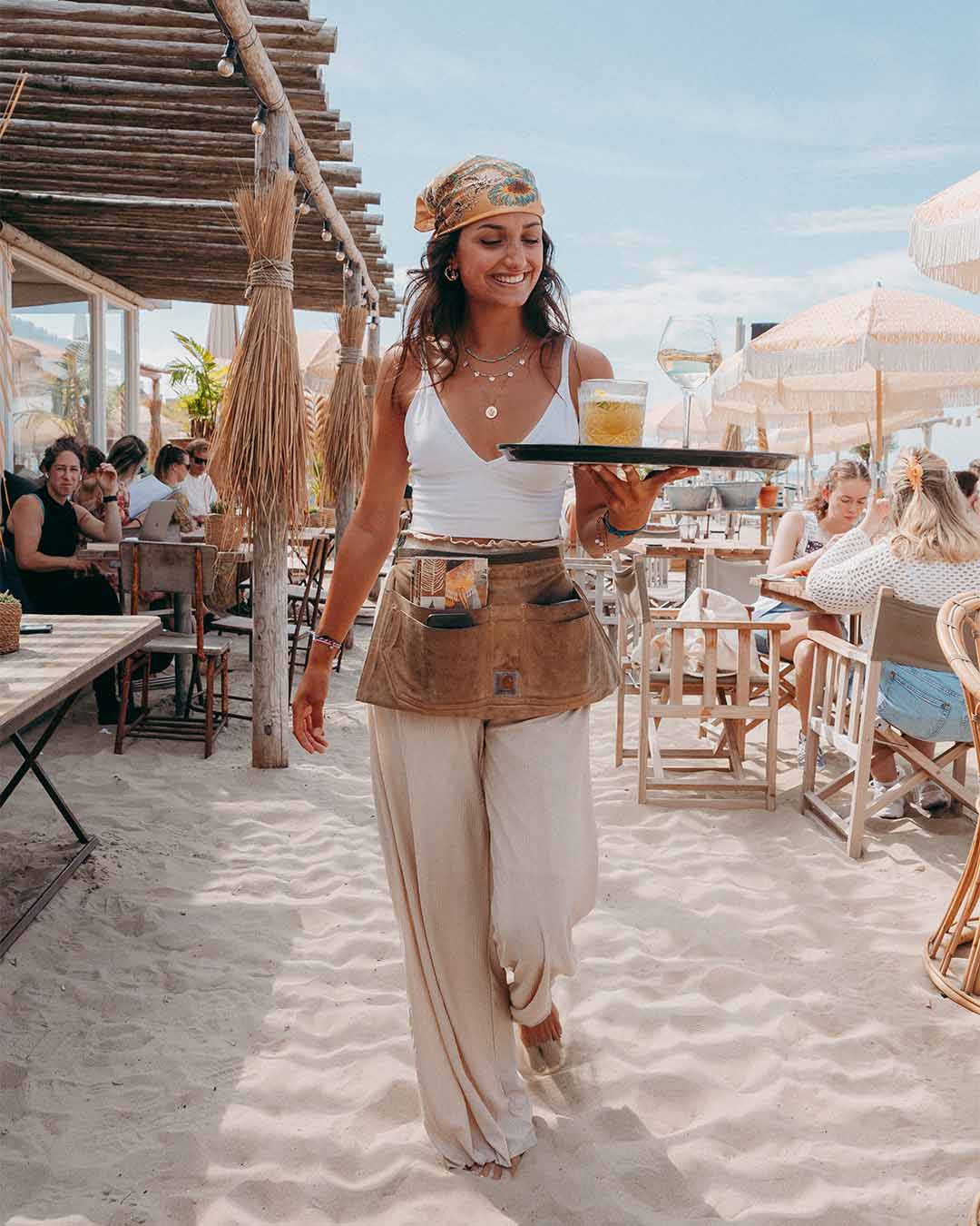 Lachend meisje lopend door het zand met dienblad met cocktails