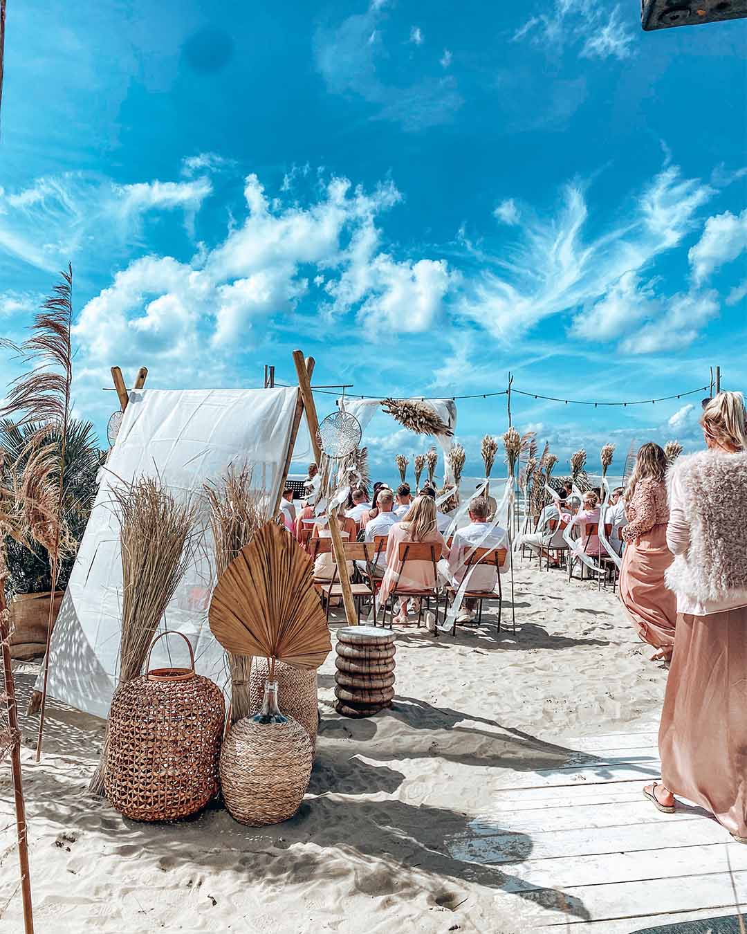 Bruiloft met bohemian decoratie in het zand onder een blauwe lucht